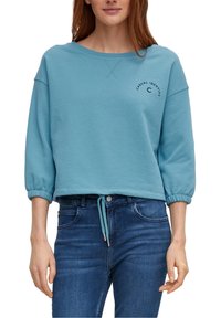 Sweatshirt bleu clair à manches trois-quarts, avec des poignets élastiques et un cordon de serrage à l'ourlet. Il arbore un logo imprimé sur le devant.