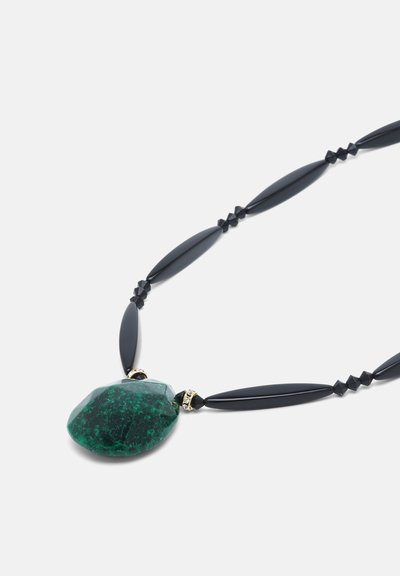 Collier avec des perles noires allongées et un grand pendentif en pierre verte foncée irrégulière placé près du centre sur un fond clair.