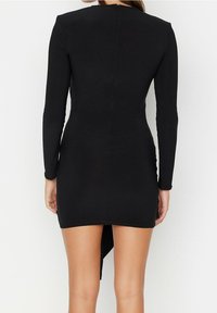 Abito lungo nero a maniche lunghe con design aderente, texture liscia e orlo asimmetrico, dotato di una zip nascosta sulla schiena.