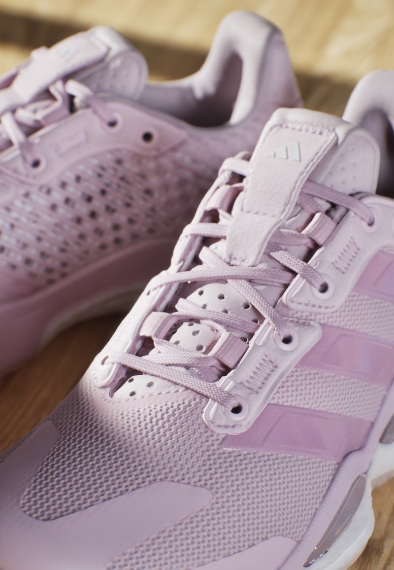 Zapatillas deportivas moradas con parte superior de malla, superficie texturizada, diseño de cordones y tres franjas de acento en el costado.