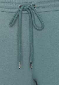 Teal joggerbyxor har en slät yta och dragsko med flätad snodd, silverfärgade metallagletter och en enkel design.