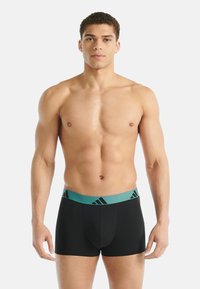 Černé boxerky s tyrkysovým pasem, na kterém je logo Adidas. Materiál působí hladce a elasticky, navržený pro pohodlí.