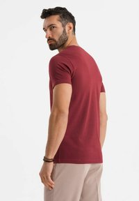 Burgundské tričko s krátkým rukávem, vyrobené z bavlny, s těsným střihem, hladkou texturou a kulatým výstřihem, nošené s světle zbarvenými kalhotami.