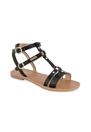 Sandale plate noire avec plusieurs fines lanières, boucles dorées sur les brides de cheville, et petits clous carrés sur la lanière centrale, semelle beige.