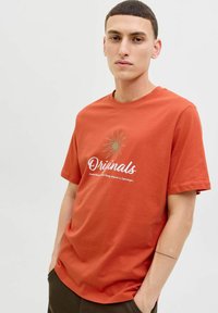 Rustfarvet bomulds T-shirt med korte ærmer og rund halsudskæring. Har et grafisk print med teksten "Originals" i hvidt og guld.