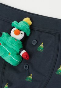 Tmavě modré bavlněné boxerky s motivem vánočních stromků, na pásku připevněná plyšová hračka tučňáka v zeleném kabátku a žluté čepici.