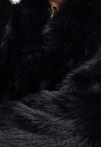 Černý šál z umělé kožešiny s měkkým, strukturovaným povrchem. Má měděnou sponu u krku, která zdůrazňuje luxusní design.