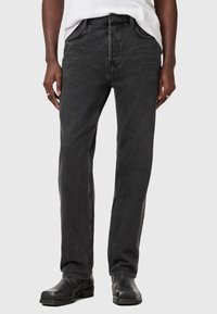 Sorte denimjeans med lige ben, fem lommer og knaplukning. Let slidte tekstur med kontrast søm; båret sammen med sorte sko.