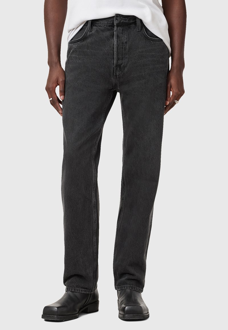 Sorte denimjeans med lige ben, fem lommer og knaplukning. Let slidte tekstur med kontrast søm; båret sammen med sorte sko.