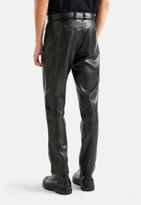 Svarta läderbyxor med en mjuk textur, med rak passform, två bakfickor och midja med bälteshällor. Stylad med svarta stövlar.