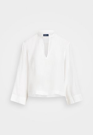 Biała lniana bluzka ze stójką, dekoltem w kształcie litery V i rękawami o długości trzy czwarte. Charakteryzuje się luźnym fasonem i skróconym dołem.