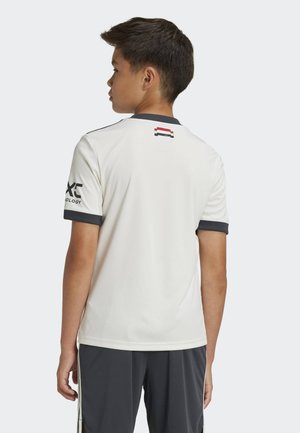 Fehér sportpóló szürke részletekkel, rövid ujjú, és egy kis grafika a hátsó részén. Az anyag könnyűnek és simának tűnik.