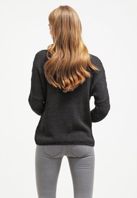 Maglione nero lavorato a maglia con una vestibilità rilassata, orlo a costine e maniche lunghe, abbinato a jeans aderenti grigio chiaro. La texture appare morbida e spessa.