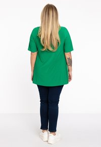 Groene tuniek top met korte mouwen en een relaxte pasvorm, gecombineerd met donkerblauwe skinny jeans en witte sneakers. Eenvoudig ontwerp zonder zichtbare patronen.