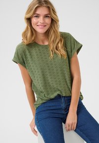 Top verde a maniche corte con un motivo a occhio di pernice testurizzato, vestibilità rilassata e scollatura rotonda, abbinato a jeans blu.