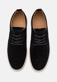 Schwarze Wildleder-Schnürschuhe mit einer glatten Textur, kontrastierenden Nähten und einer braunen Innensohle mit geprägtem Branding. Gummisohle.