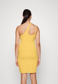 Vestido amarelo assimétrico com uma alça, design justo, textura suave e comprimento até a metade da coxa. A parte de trás apresenta uma seção aberta.