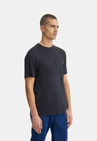 T-shirt in cotone nero con collo a giro, maniche corte e un piccolo logo sul lato sinistro del petto. Tessuto liscio, vestibilità comoda.