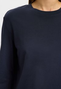 Tamnoplava majica dugih rukava od mekog pamuka, s okruglim izrezom i glatkom teksturom, bez vidljivih uzoraka ili naglasaka.