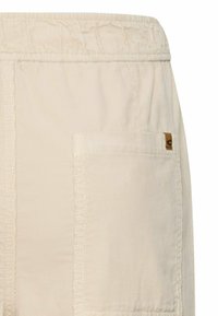 Beige cargoshorts met een elastische tailleband, voorzien van een opgestikte zak en zichtbare stiksels. Gladde stoftextuur.