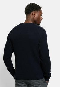 Marineblauer Strickpullover mit strukturiertem Finish, Rundhalsausschnitt und gerippten Bündchen. Verfügt über eine figurnahe Passform und dezente Nahtdetails.