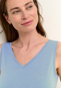 Šviesiai mėlyna trumpa palaidinė, pagaminta iš minkštos medžiagos, su V formos iškirpte, švariais linijomis ir lygiu paviršiumi. Paprastas ir universalaus stiliaus.