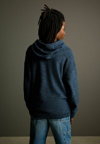Sudadera de punto azul marino con un acabado texturizado, que cuenta con una gran capucha y puños acanalados. Combinada con unos pantalones cargo azul claro.