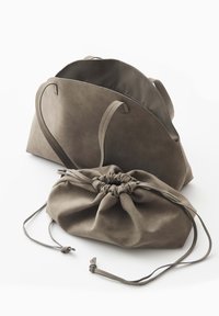 Twee taupekleurige tassen: een gestructureerde handtas met handvatten en een zachte stoffen zak met trekkoord, beide met een gladde, matte afwerking.