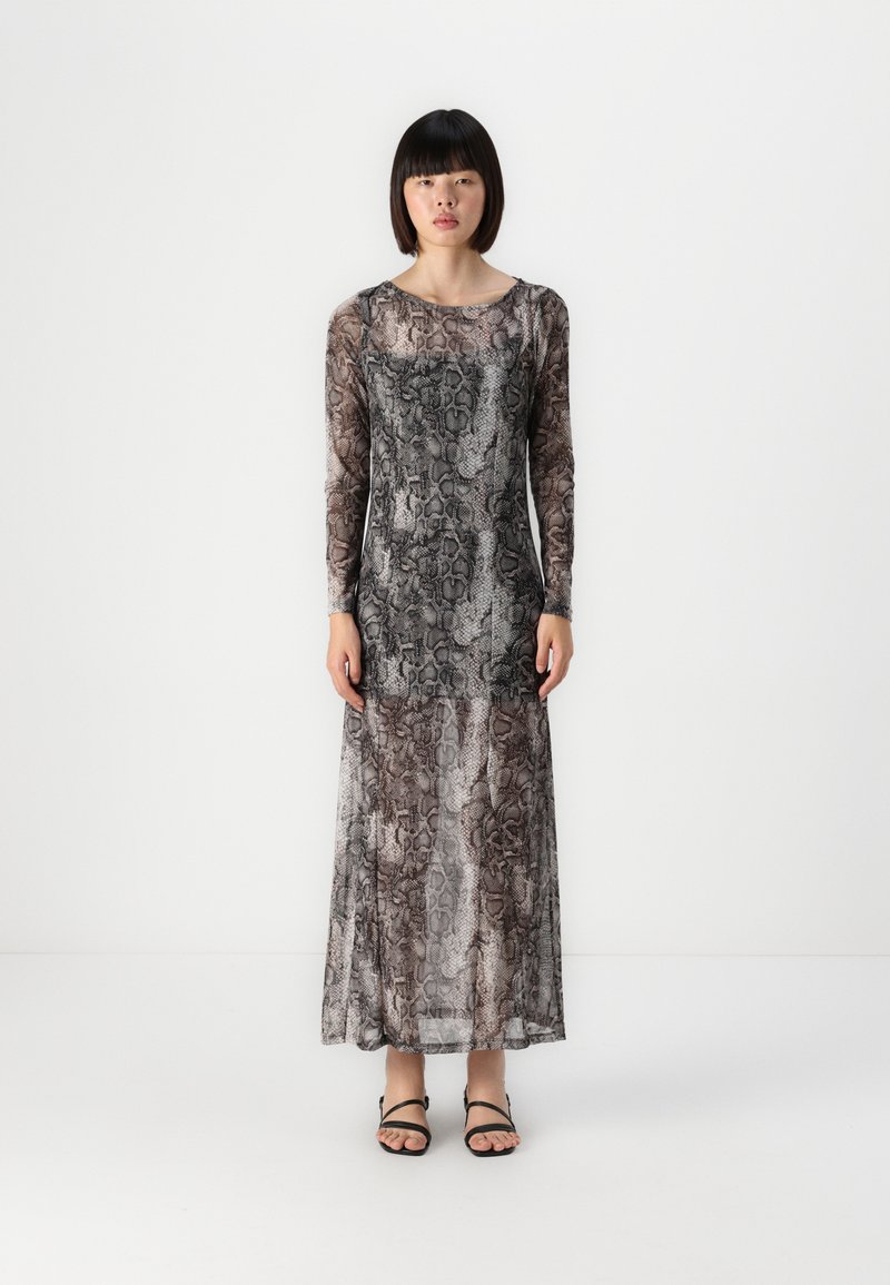 Dolga obleka z vzorcem kače v odtenkih sive in rjave. Prozoren, lahkoten material seže do gležnjev, v kombinaciji s črnimi sandali.