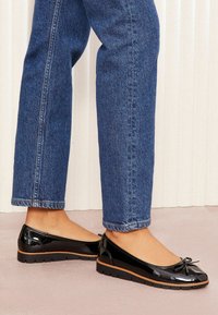Mustad lakknahk kingad ümmarguse varbaga, lipsudetailiga ja tekstureeritud tallaga, kombineeritud siniste lühikeste denim pükstega.