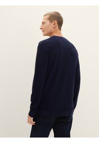 Marineblau strukturierter Pullover mit langen Ärmeln, rundem Halsausschnitt und gerippten Bündchen. Dezente Nahtdetails auf der Rückseite.
