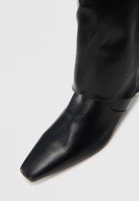 Stivale alla caviglia in pelle nera, con punta affusolata, texture liscia, design minimalista e bordo superiore leggermente piegato.