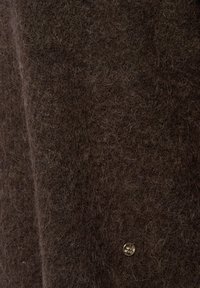 Bruine wol stof met een zachte, textuurachtige oppervlakte. Heeft een kleine, glanzende knoopdetail aan de onderzijde rechts.