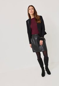 Mustat bleiseri burgundinvärisen topin päällä, yhdistettynä muotoonommeltuun mustaan nahkahameeseen ja polvipitkiin mustiin mokkabootseihin, vaalealla taustalla.