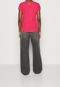 Lyserød t-shirt med korte ærmer og rund halsudskæring, kombineret med løstsiddende, blegne sorte wide-leg jeans.