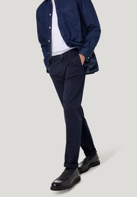 Marineblaue Baumwollhosen mit geradem Bein, kombiniert mit einem Jeanshemd und schwarzen, polierten Schuhen.