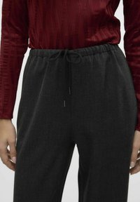 Pantalons texturés gris foncé, avec une taille élastique et un cordon de serrage ajustable. Associés à un haut ajusté en ribbed bordeaux.