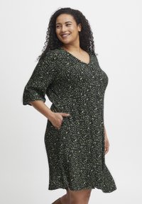 Rochie neagră cu model floral verde, decolteu în V, mâneci scurte și buzunare. Material fluid cu o croială până la genunchi.