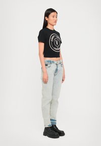 Juoda trumpa marškinėlių su apvaliu šviesiai rožiniu logotipu. Šviesiai mėlyni aukšto juosmens džinsai su nelygumais. Juodi bateliai su raišteliais.