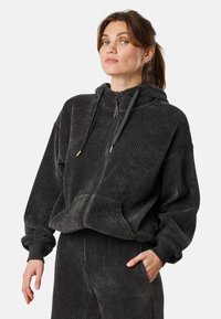 Dunkelgrauer Cord-Hoodie mit Reißverschluss, Kängurutasche und verstellbarem Kordelzug an der Kapuze. Mit gerippten Bündchen und strukturiertem Stoff.