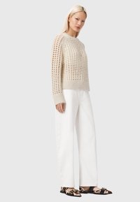 Pull beige tricoté avec un motif en treillis ouvert, poignets et ourlet côtelés, associé à un pantalon blanc à jambes larges et des chaussures à enfiler à motifs.