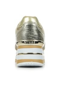 Baskets dorées métalliques avec un dessus synthétique texturé, présentant une semelle plate-forme épaisse blanche avec des rayures dorées et le logo "GUESS" au niveau du talon.