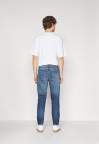 Jeans bleus en denim, coupe droite, avec poches arrières, associés à un t-shirt blanc à manches courtes et des baskets blanches.