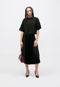 Μαύρο κοντομάνικο τοπ, πλισέ μαύρη μίντι φούστα, μυτερά μαύρα ψηλοτάκουνα, τσάντα χειρός μπορντό. Λείο ύφασμα με υφή σχεδίου.