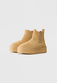 Bottines Chelsea en daim tan avec une plateforme, panneaux latéraux élastiques et languettes de tirage sur un fond blanc.