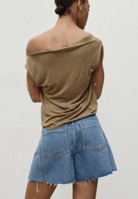 Olivgrön off-shoulder topp med draperad textur, matchad med ljusblå denimshorts med fransad nederkant och klassisk fickdesign.