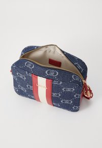 Blauer Denimtasche mit Reißverschluss, versehen mit einem rot-weiß gestreiften Akzent und einem Logodetail. Innenfutter aus beigem Stoff.
