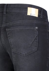 Jeans de denim negro con un bolsillo trasero de forma única y una etiqueta marrón con rayas blancas en la cintura, destacando los detalles de costura.