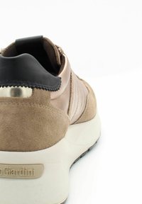 Beige suède sneaker met satijnen accenten, zwarte hieltab, gladde textuur en witte zool. Bevat een metallic logo aan de zijkant.
