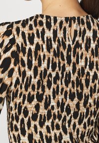 Tessuto con stampa leopardata nei colori nero e sabbia. Presenta una superficie testurizzata e un'apertura a chiave sul retro con una piccola chiusura a bottone.